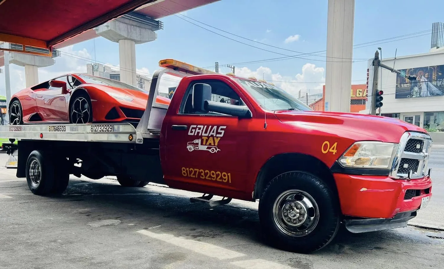 Camión de plataforma GRUAS TAY cargando un auto deportivo rojo en una estación de servicio