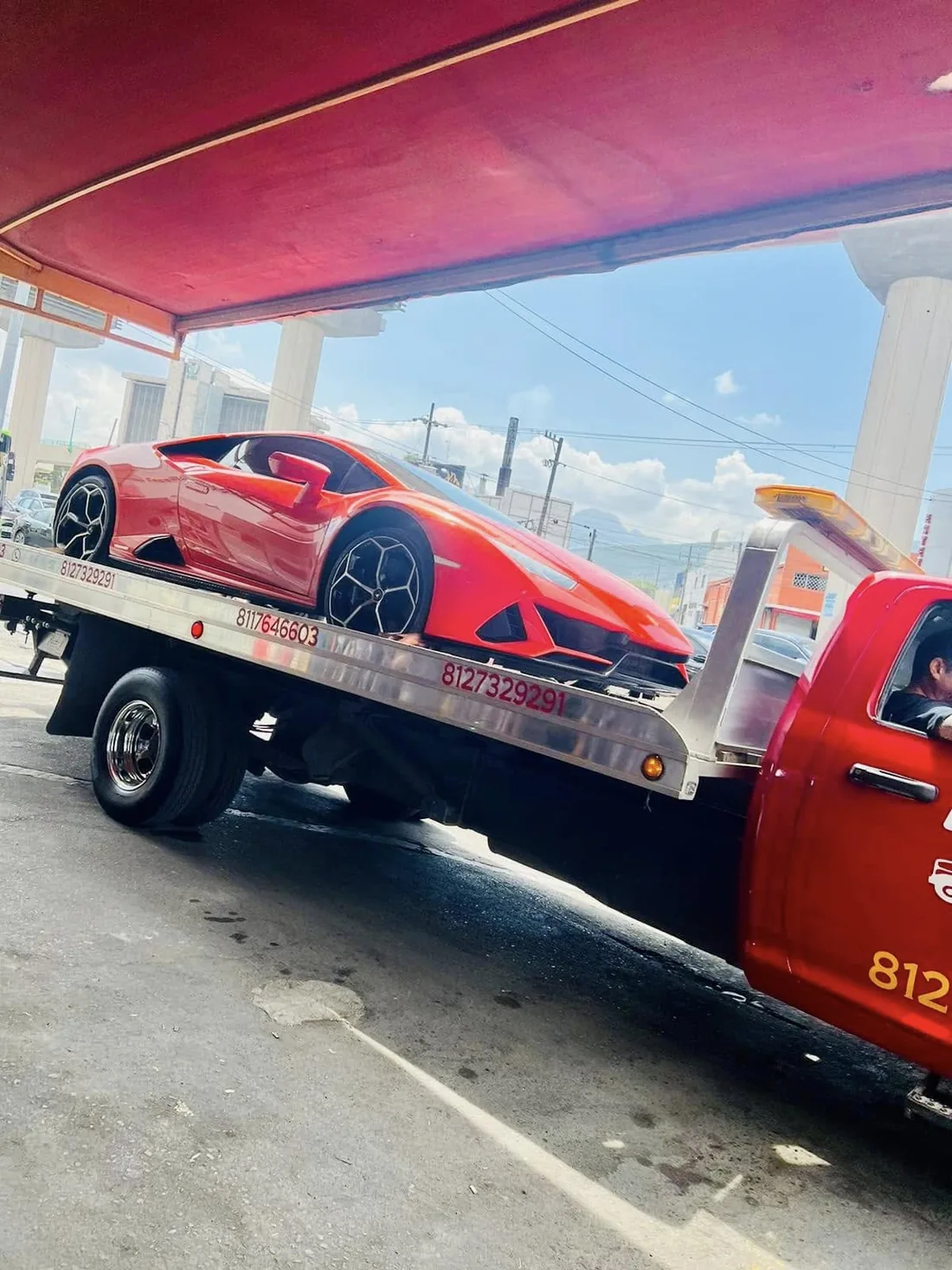 Auto deportivo rojo subido a la plataforma de la grúa bajo una estructura roja